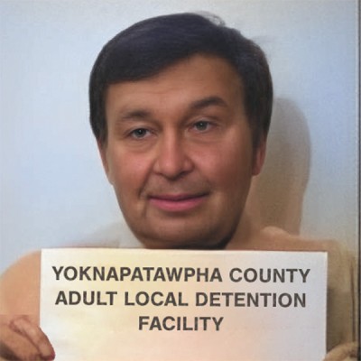 Older man with short dark hair holding a jail booking card